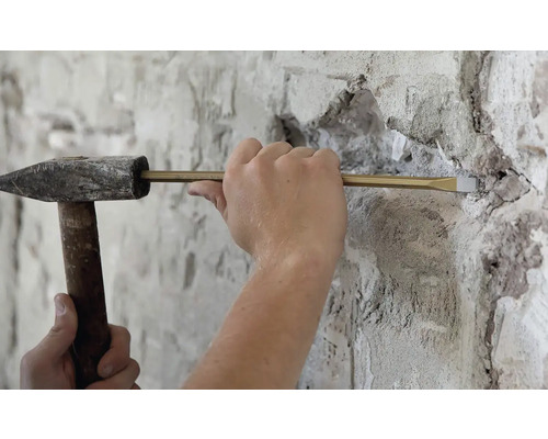 Nahaufnahme einer Person, die mit einem Hammer und einem Meißel an einer Wand arbeitet