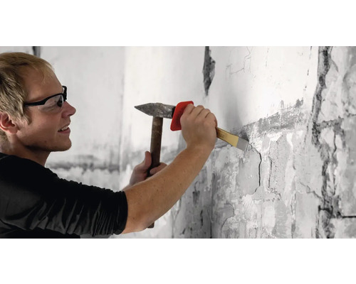 Ein Mann stemmt mit Hammer und Meißel eine Wand auf