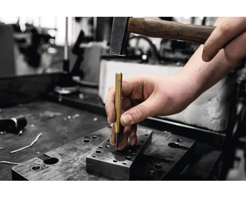 Ein Mann verwendet einen Hammer und einen Durchschlag auf einer Werkbank.