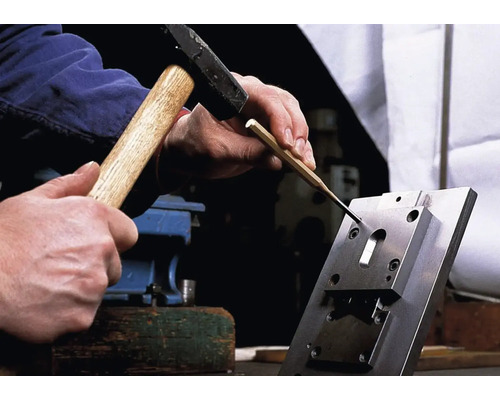 Ein Mann benutzt einen Hammer und einen Durchschlag auf einem Werkstück.