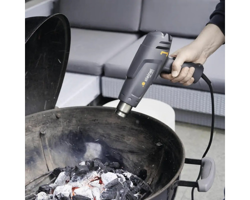 Person zündet Grillkohle mit einem Heißluftfön von Steinel an.