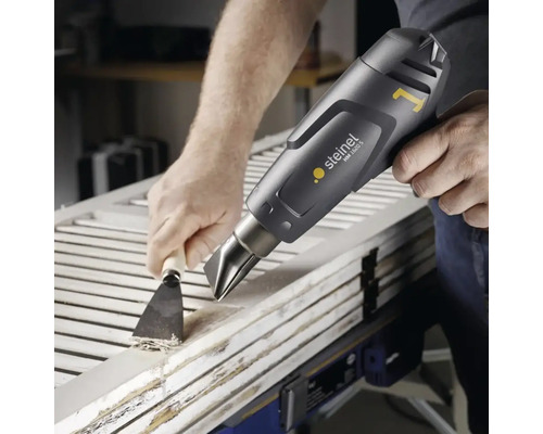 Handwerker entfernt Farbe von einer Holztür mit einem Heißluftfön und einem Spachtel