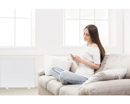 Frau sitzt mit Smartphone auf Sofa neben Heizkörper