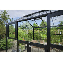 Gewächshaus mit Glaswänden und Metallrahmen, eingerichtet mit Tisch und Stühlen.