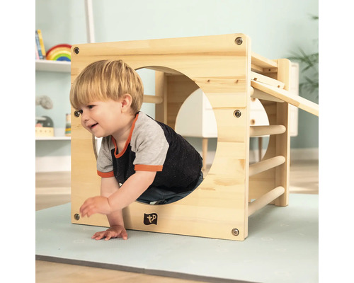 Kind klettert durch einen Holzspielwürfel mit Sprossen und einer Rutsche im Kinderzimmer.