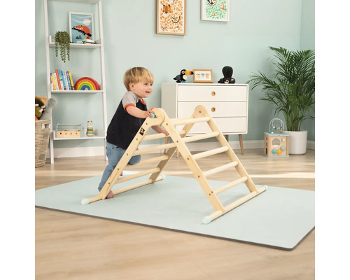 Kind klettert auf einem Indoor-Klettergerüst aus Holz auf einer Spielmatte im Kinderzimmer.