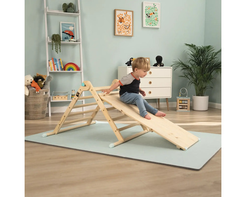 Kind spielt auf einem hölzernen Kletterdreieck mit Rutsche im Kinderzimmer.