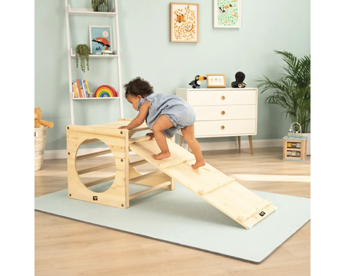 Kleinkind klettert auf ein Holzspielgerät mit Rutsche in einem Kinderzimmer