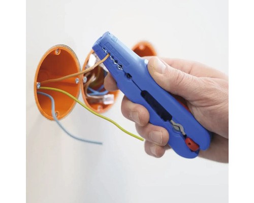 Eine Person verwendet eine Abisolierzange, um ein Kabel freizulegen. Im Hintergrund sind zwei orangefarbene Verteilerdosen zu sehen.