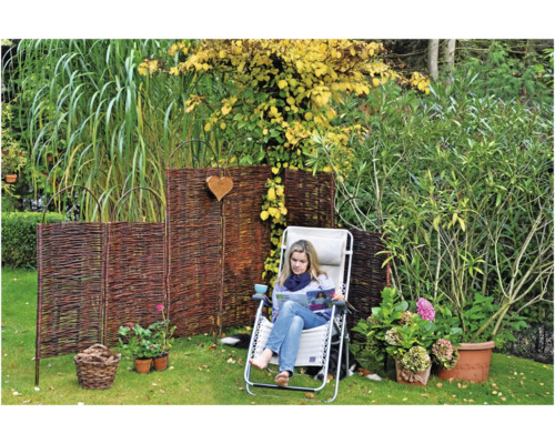 Gartenszene mit Weidenzaun, Liegestuhl und Frau beim Lesen im Garten