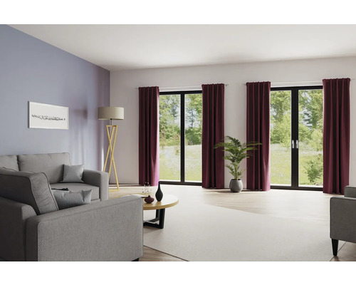 Wohnzimmer mit Sofa, Stehlampe, Couchtisch, Zimmerpflanze und Vorhängen vor Fenstern.