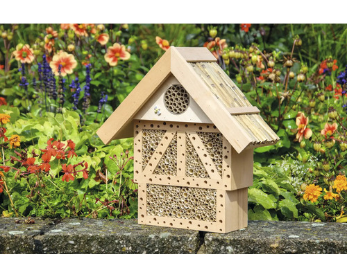 Insektenhotel aus Holz mit Bambusröhren vor blühendem Hintergrund