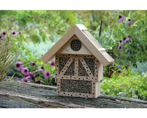Insektenhotel aus Holz mit Röhren vor Gartenkulisse