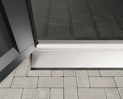 Detailansicht eines Schwellenprofils zwischen einer Tür und Pflastersteinen.