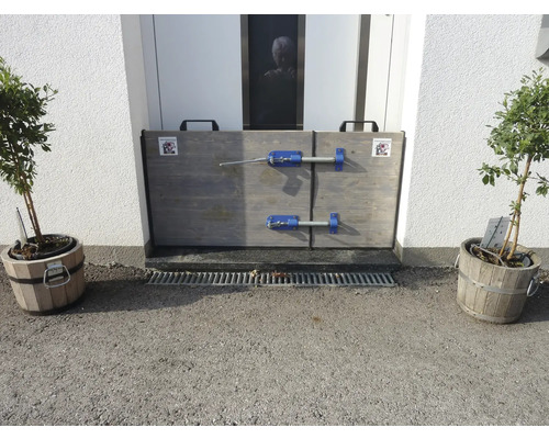 Installierte Hochwasserschutzvorrichtung vor einer Haustür, flankiert von zwei Topfpflanzen