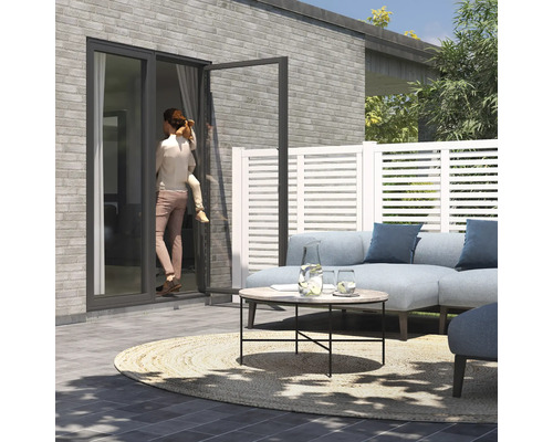 Terrasse mit Loungemöbeln, Zaunelementen und einer Frau mit Kind an einer Terrassentür