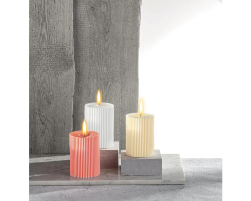 Drei gerippte Stumpenkerzen in verschiedenen Farben auf Betonblöcken
