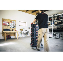 Eine Person schiebt einen Werkzeugkofferwagen mit mehreren Boxen in einer Werkstatt.