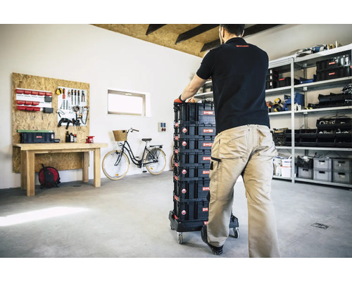 Eine Person schiebt einen Werkzeugkofferwagen mit mehreren Boxen in einer Werkstatt.