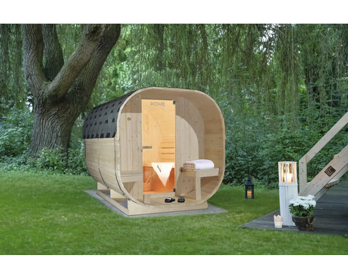 Saunahaus Home Deluxe Cube Deluxe L inkl. 8 kW u.integr.Steuerung mit Ganzglastüre aus Klarglas Holzfasssauna im Garten mit Baum und Gartenbeleuchtung