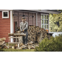 Mann sägt Holz mit einer Kettensäge vor einem Holzhaus