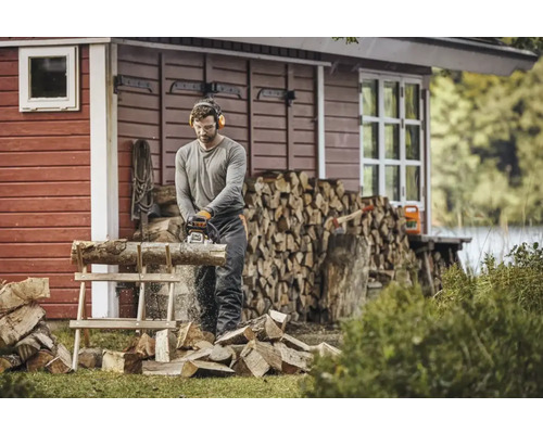 Mann sägt Holz mit einer Kettensäge vor einem Holzhaus