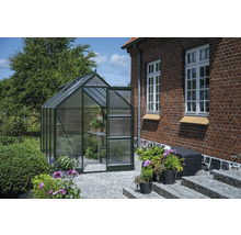 Gewächshaus mit geöffneter Tür in einem Garten neben einem Backsteingebäude.