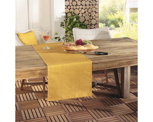 Szene mit einem Esstisch im Freien mit Tischläufer, Brot, Weintrauben und einem Glas Wein.