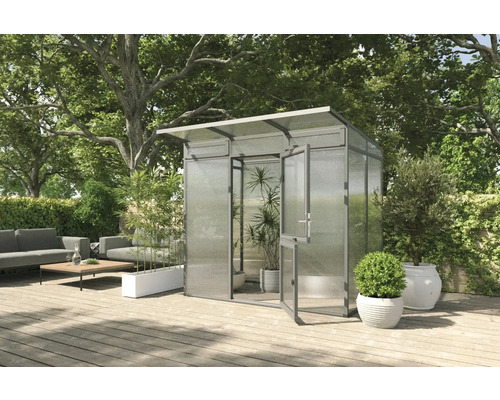 Gewächshaus mit geöffneter Tür auf einer Terrasse mit Gartenmöbeln und Bepflanzung.