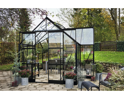 Gewächshaus mit Glaswänden und Pflanzen im Garten.