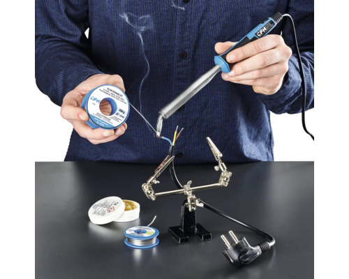 Elektrolötkolben CFH E 100 Person lötet mit Lötkolben, Lötzinn und Lötfett Kabel auf einer Arbeitsfläche.