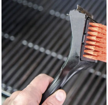 Eine Grillbürste mit Schaber reinigt einen Grillrost.