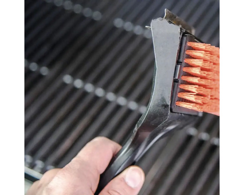 Eine Grillbürste mit Schaber reinigt einen Grillrost.