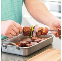 Mann spießt Fleisch und Gemüse auf einen Grillspieß über einer Schale mit Fleischstücken