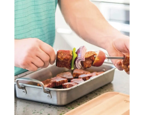 Mann spießt Fleisch und Gemüse auf einen Grillspieß über einer Schale mit Fleischstücken
