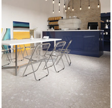 Innenraum mit Terrazzoboden, weißen Tischen und transparenten Stühlen.