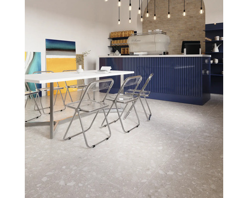 Innenraum mit Terrazzoboden, weißen Tischen und transparenten Stühlen.