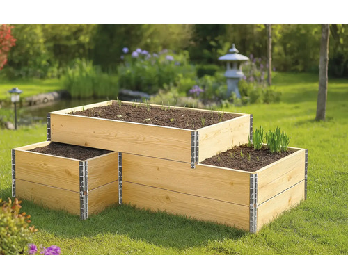 Dreistufiges Hochbeet aus Holz im Garten mit Erdreich und jungen Pflanzen.
