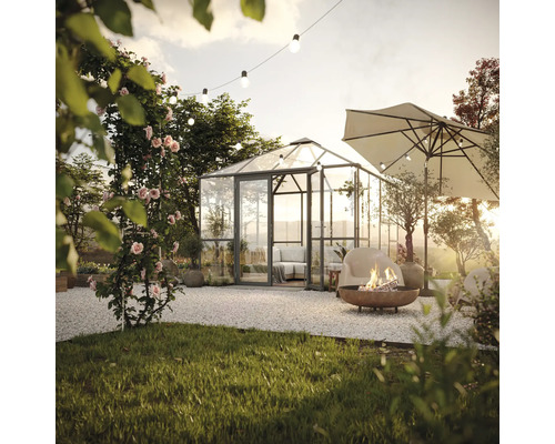 Gartenszene mit Gewächshaus, Sitzbereich, Sonnenschirm und Feuerstelle