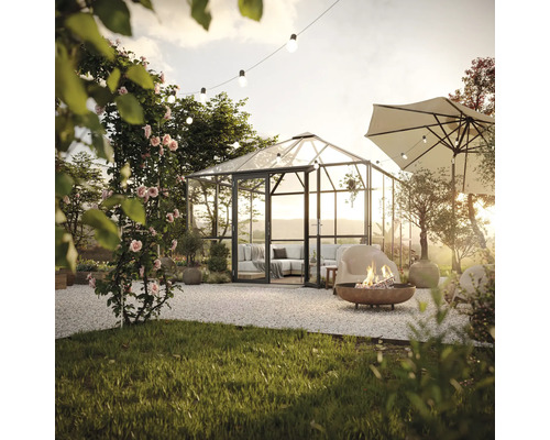 Gartenszene mit Gewächshaus, Feuerstelle und Sonnenschirm auf Kiesfläche