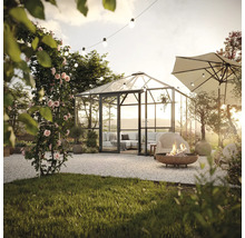 Gartenszene mit Gewächshaus, Feuerstelle und Sonnenschirm auf Kiesfläche