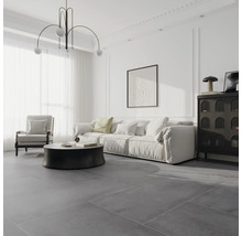 Modernes, helles Wohnzimmer mit großformatigen, grauen Bodenfliesen, weißem Sofa, schwarzem Rundtisch und minimalistischer Pendelleuchte.