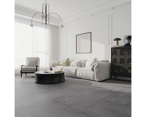 Modernes, helles Wohnzimmer mit großformatigen, grauen Bodenfliesen, weißem Sofa, schwarzem Rundtisch und minimalistischer Pendelleuchte.