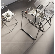 Raumszene mit zwei transparenten Stühlen, einem Beistelltisch mit Lampe, Tasse, Apfel und Zeitschriften auf einem grauen Boden.