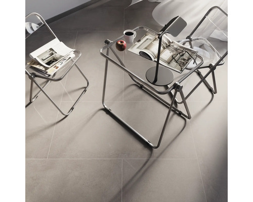 Raumszene mit zwei transparenten Stühlen, einem Beistelltisch mit Lampe, Tasse, Apfel und Zeitschriften auf einem grauen Boden.