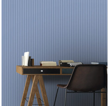 Arbeitszimmer mit Schreibtisch, Büchern, Schreibmaschine und Stuhl vor einer Wand mit vertikalem Streifenmuster