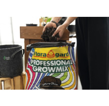 Eine Person schaufelt Blumenerde aus einem Sack Floragard Professional Growmix. Daneben steht ein grauer Pflanzbehälter.