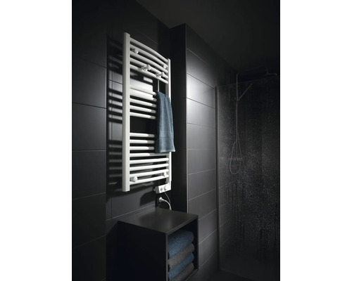 Moderner weißer Handtuchheizkörper an einer dunklen Fliesenwand neben einer Glasdusche in einem Badezimmer.