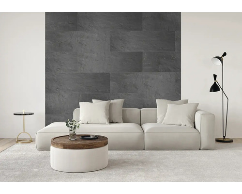 Modernes Wohnzimmer mit einer Akzentwand aus großformatigen, dunkelgrauen Wandverblendern in Natursteinoptik hinter einem hellen Sofa.