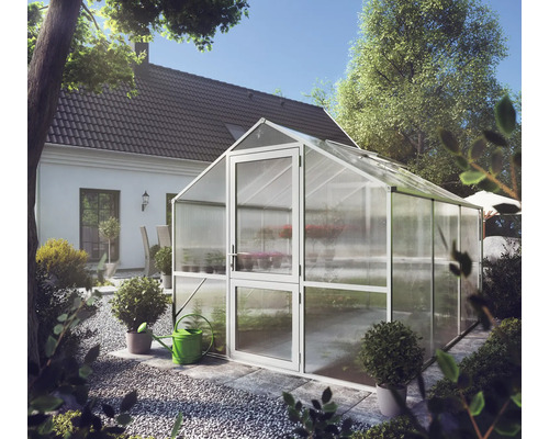 Modernes Gewächshaus mit Metallrahmen und transparenten Platten in einem hellen, organisierten Garten neben einem Wohnhaus.